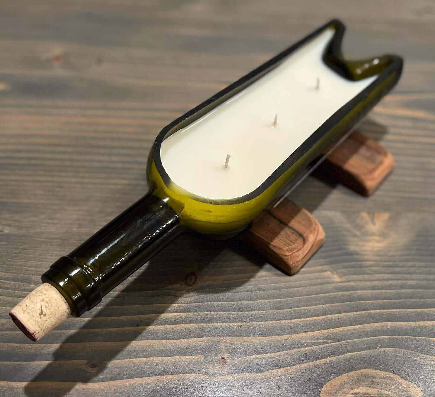 Long Cut Candle with three wicks in a repurposed green bottle on handcrafted wooden stands