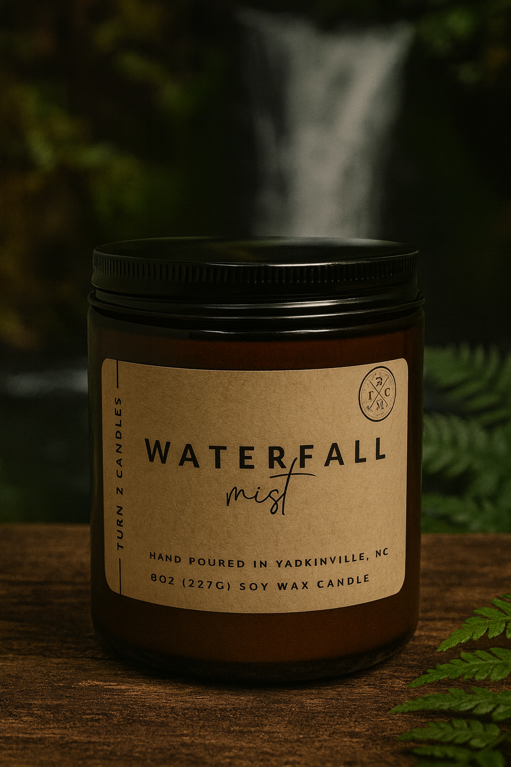 Hand-poured soy wax candle in an amber jar labeled “Waterfall Mist,” set on a wooden surface with green foliage and a waterfall blurred in the background.