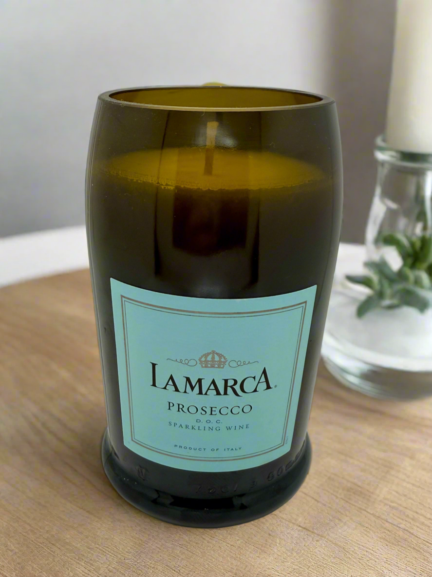 Candle in a bottle labeled 'Lamarca Prosecco' on a wooden surface.