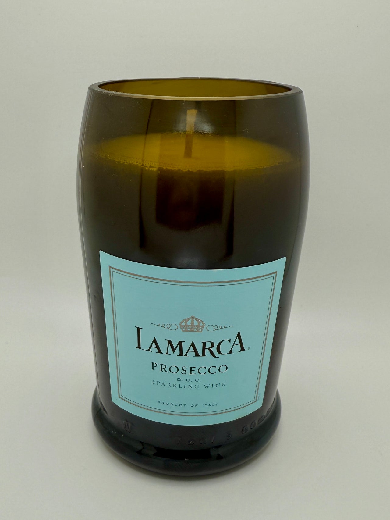 Candle in a bottle labeled 'Lamarca Prosecco' on a white background