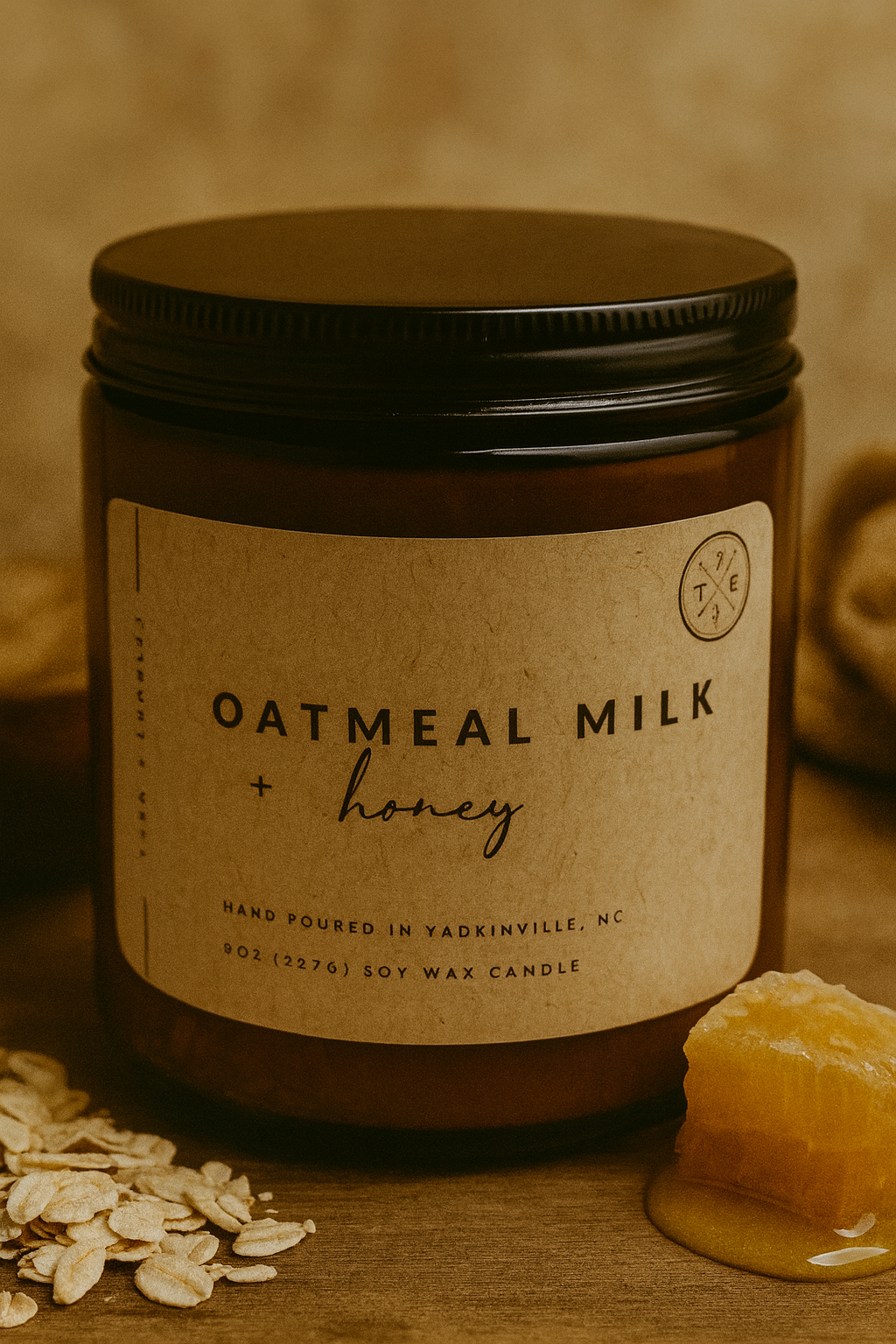 Candle jar labeled 'Oatmeal Milk + Honey' with oats and honeycomb on a wooden surface.